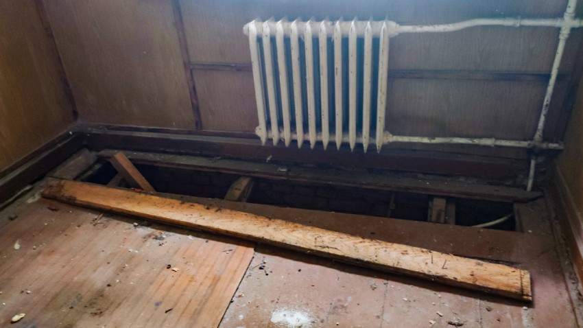 Разобранный деревянный пол и радиатор отопления в заброшенном помещении