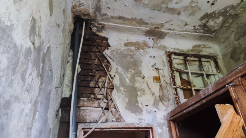 Крупный план разрушенной стены с дранкой, трубой и ржавой рамой окна под потолком