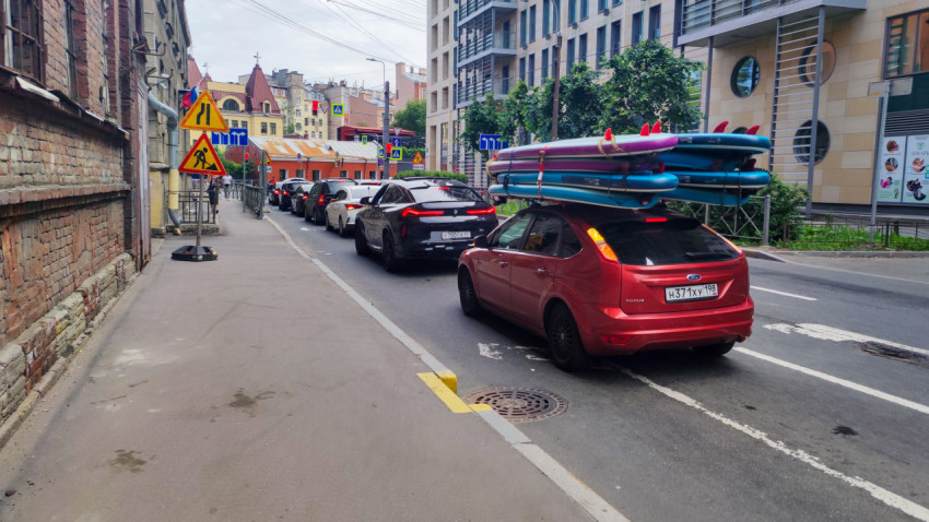 Красный Ford Focus с надувными SUP-досками на крыше стоит в пробке на городской улице