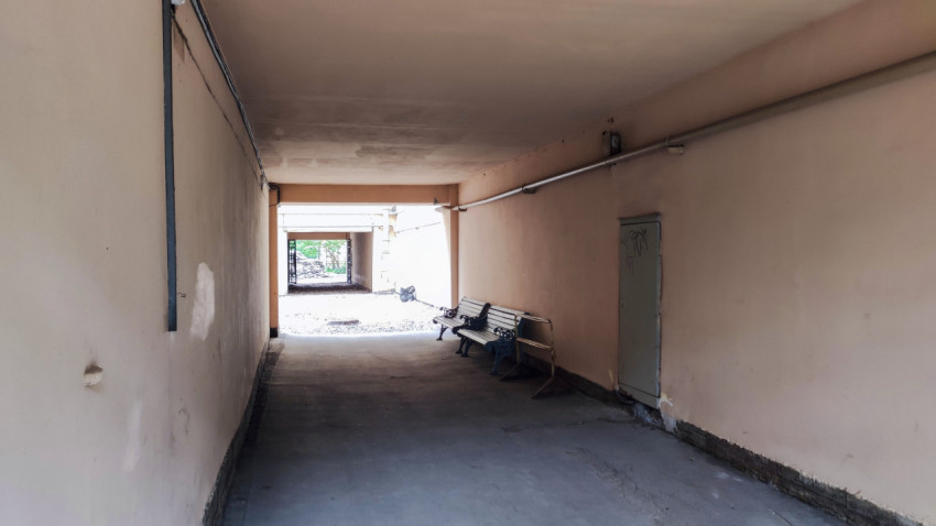 Проход под аркой жилого дома с лавочками, дверью и инженерными коммуникациями