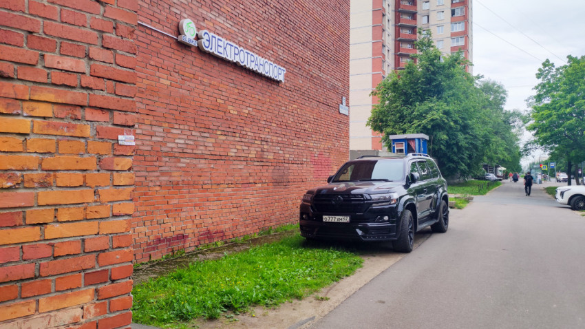 Кирпичная стена с вывеской «Электротранспорт» и припаркованный внедорожник у тротуара