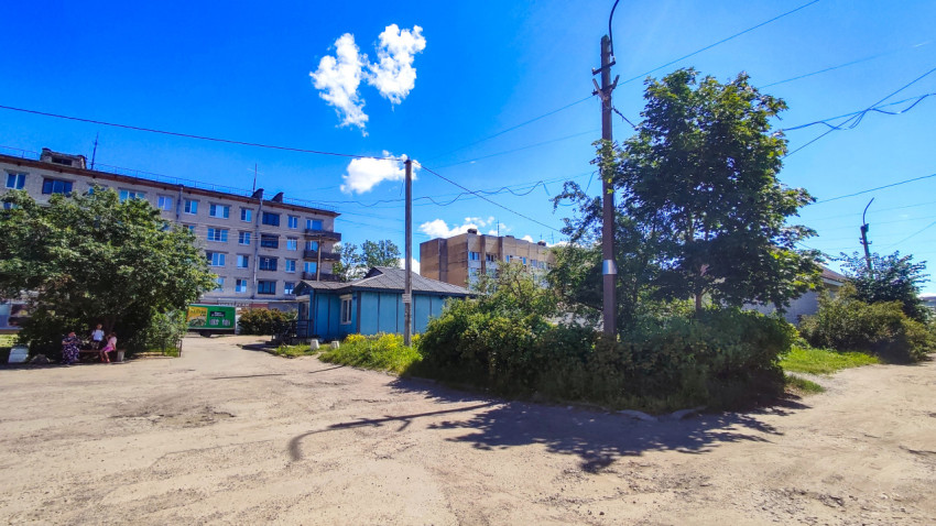 Дворовой проезд с грунтовым покрытием, кустами и многоэтажными домами под проводами