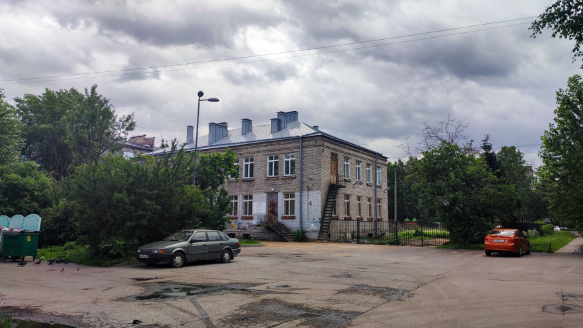 Двухэтажное кирпичное здание с металлической кровлей и наружной лестницей у дворового проезда