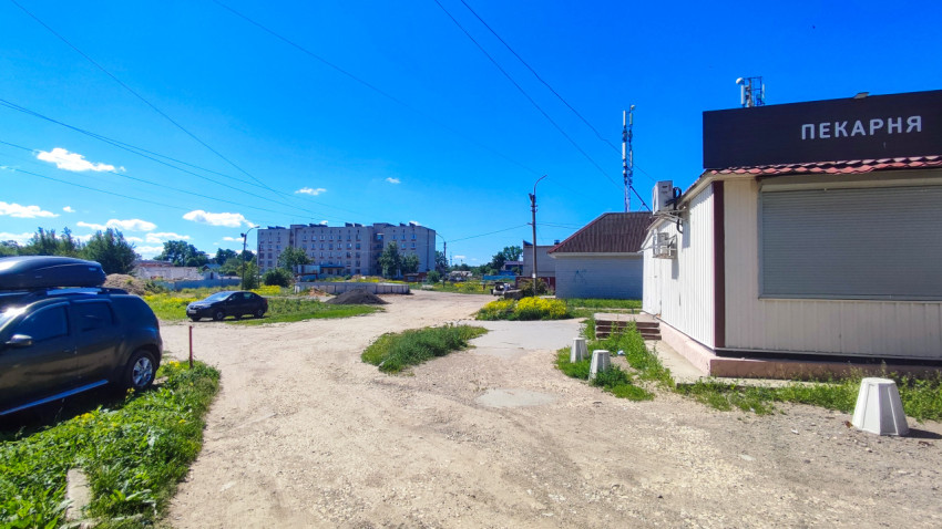 Киоск «Пекарня» у грунтового проезда и жилых домов на заднем плане