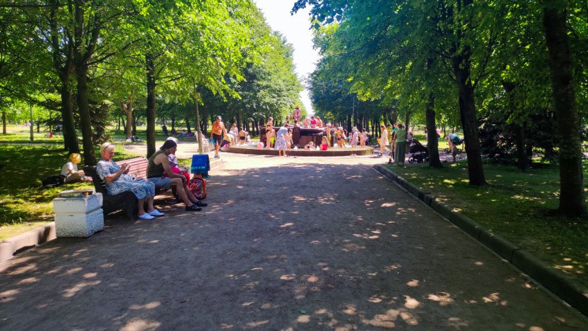 Аллея городского парка ведёт к фонтану, где дети играют в воде в жаркий день