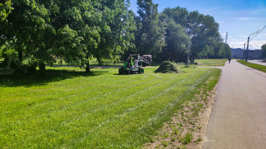 Коммунальный рабочий на газонокосилке рядом с кучей скошенной травы