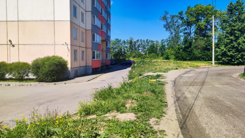Проезд у торца многоэтажного дома рядом с пустырем и лесополосой