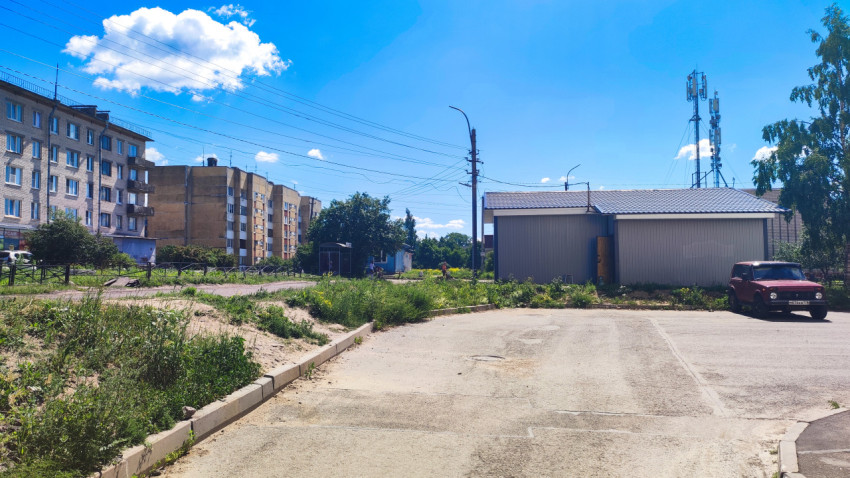Пустая асфальтовая площадка у металлического ангара и жилых домов