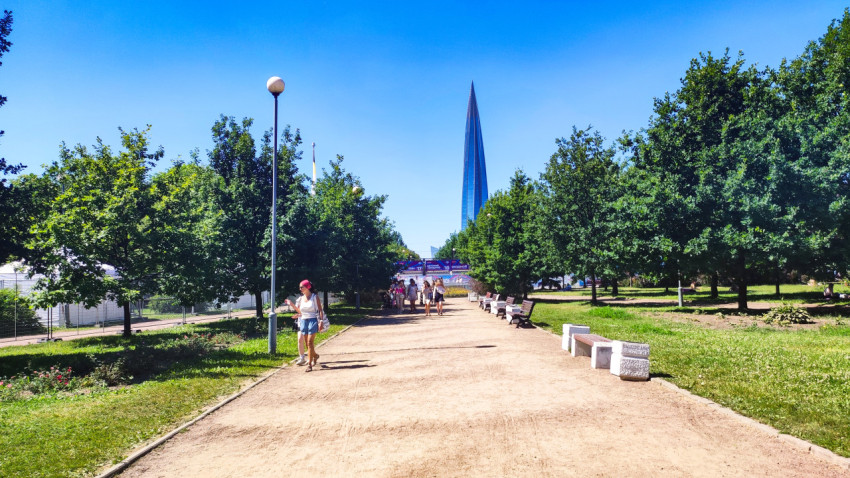 Прогулочная дорожка с лавочками и пешеходами на фоне небоскрёба Лахта Центр в Санкт-Петербурге