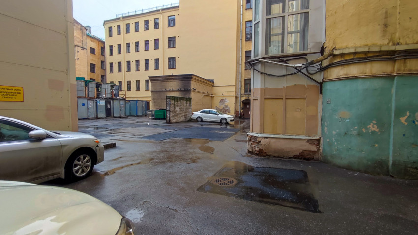 Внутренний двор с хозблоком, временными ограждениями, лужами и припаркованными автомобилями