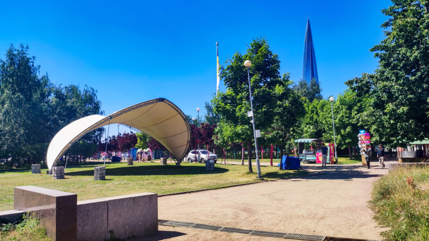 Тентовый навес в парке у пешеходной дорожки на фоне шпиля небоскреба
