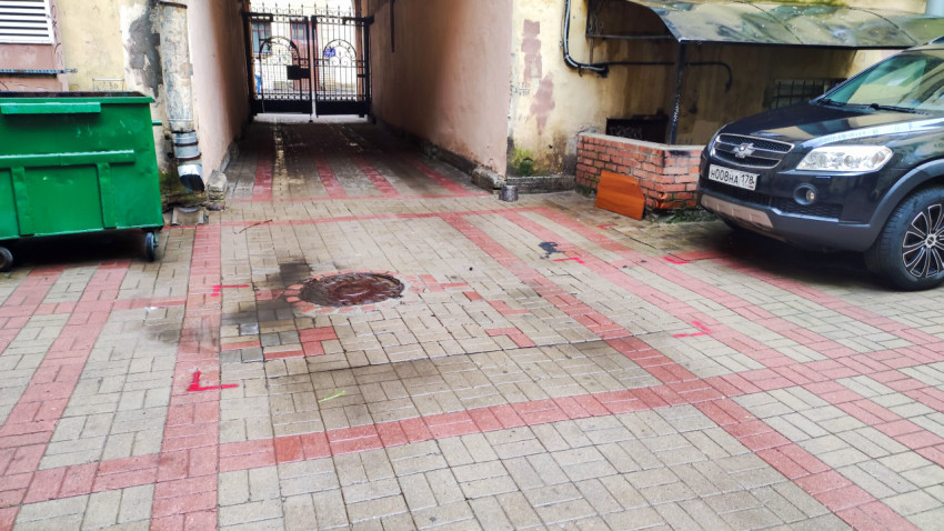 Проезд во двор с решетчатыми воротами, мусорным контейнером и люком на плитке