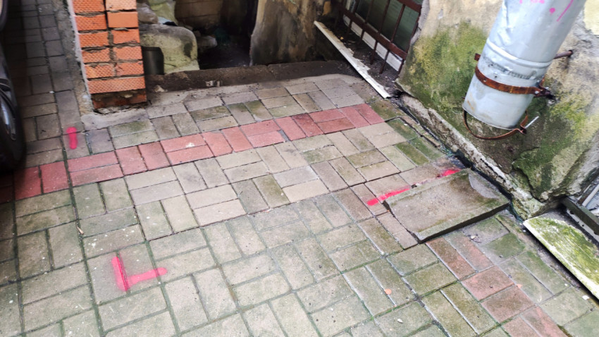 Участок двора у подвального окна с водосточной трубой, сырой стеной и разметкой на плитке