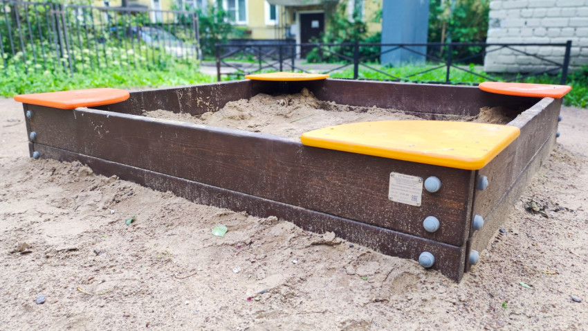 Крупный план деревянной песочницы с пластиковыми сиденьями и табличкой-паспортом