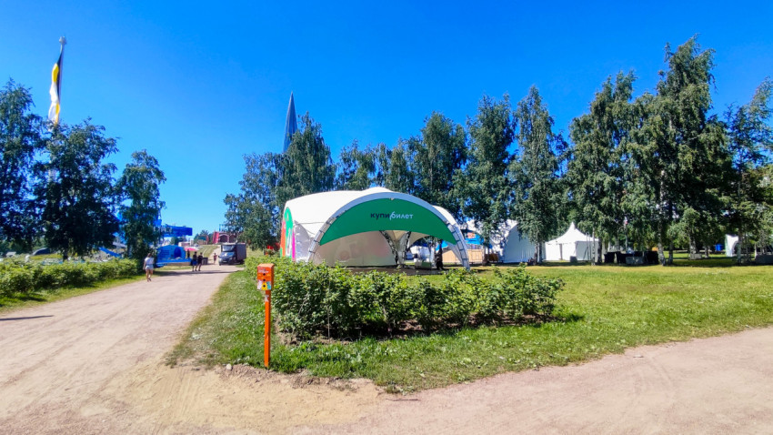 Фестивальная поляна с аркой «купи билет», шатрами и грунтовыми дорожками в парке