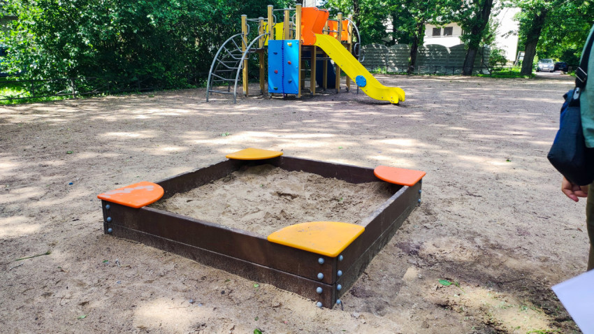 Песочница и игровой комплекс на дворовой детской площадке среди деревьев