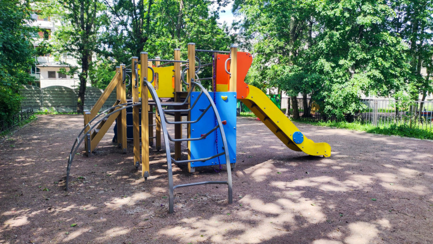 Яркий игровой комплекс с горкой и лазалками на площадке в тенистом дворе