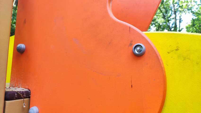 Изношенная оранжевая панель детского игрового оборудования с крепежным болтом