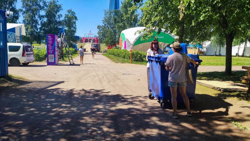 Волонтеры с контейнером для мусора на фестивальной дороге среди шатров и техники