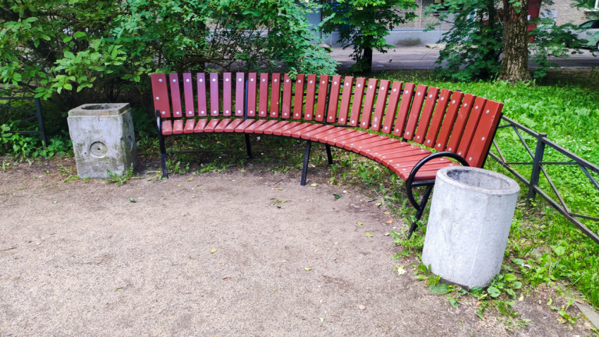 Изогнутая красная скамейка и бетонные урны в зелёном дворе