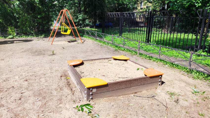 Песочница и качели на пустой детской площадке во дворе