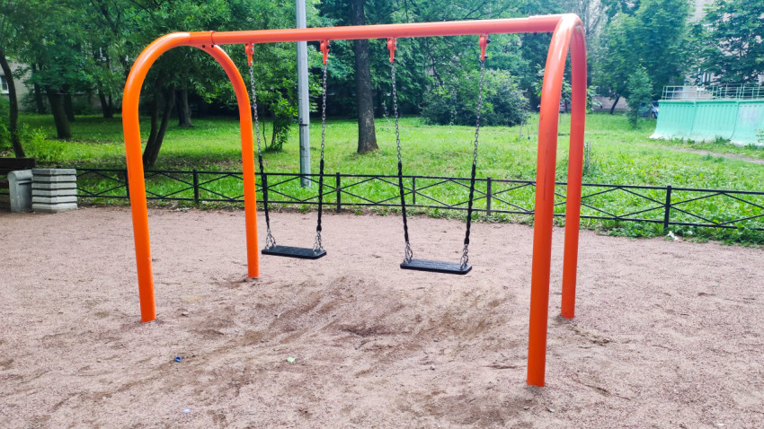 Оранжевые дворовые качели с двумя сиденьями на песчаной площадке