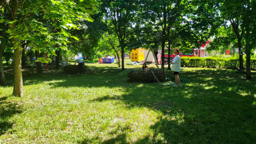 Подготовка площадки в парке с рабочими, лестницей, ветками и торговыми павильонами на фоне