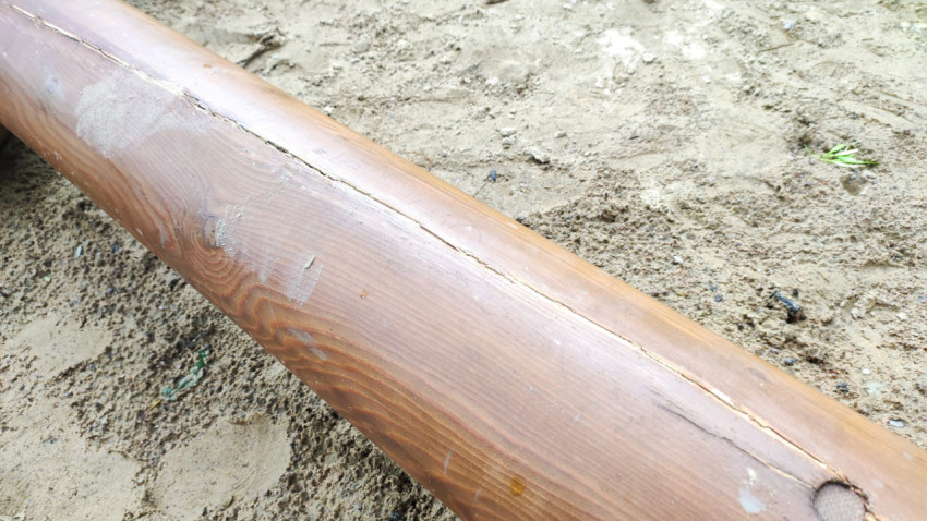 Фактура деревянного бруса с трещиной на песчаном основании детской площадки