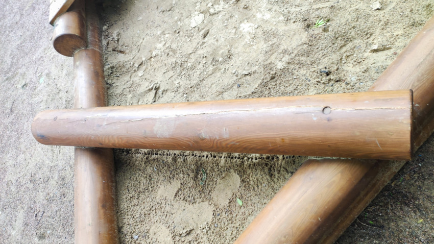 Деревянное бревно песочницы с продольной трещиной и следами износа