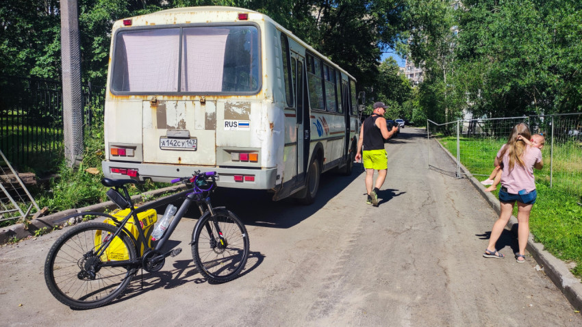 Старый автобус на узкой дороге в зелёном районе рядом с велосипедом и прохожими