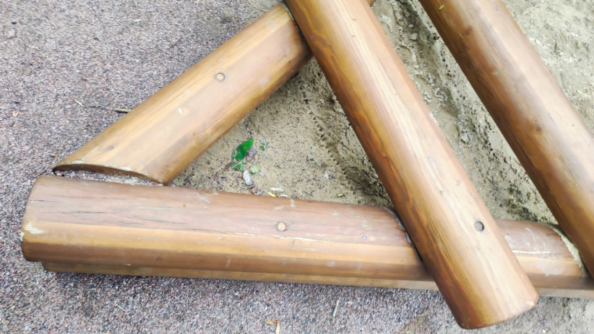 Сложенные брёвна от песочницы на резиновом покрытии рядом с песком