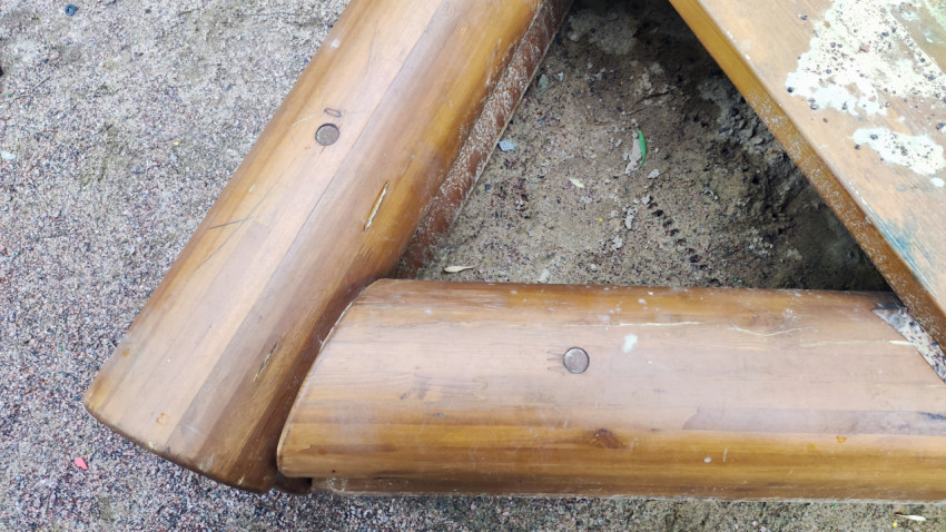 Угловое соединение брёвен песочницы с деревянными заглушками и следами эксплуатации