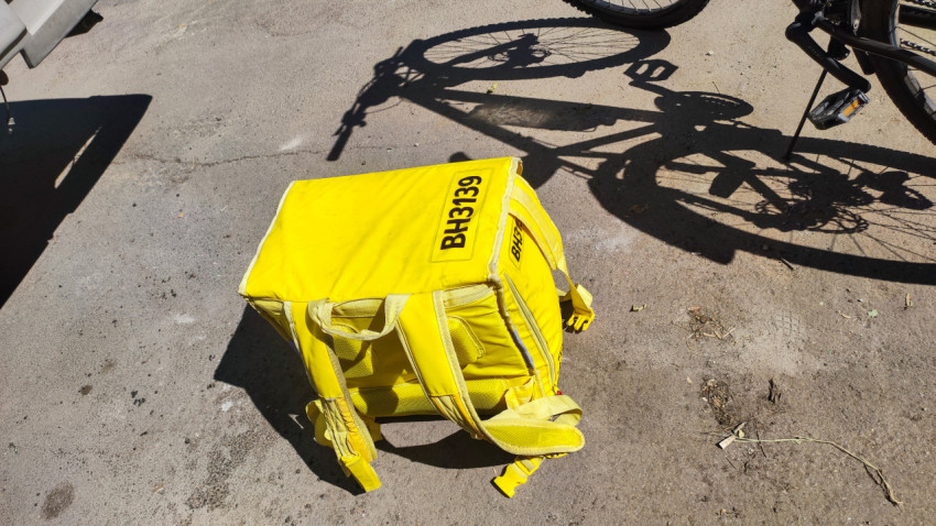 Жёлтый рюкзак курьера с маркировкой BH3139 на асфальте рядом с тенью велосипеда