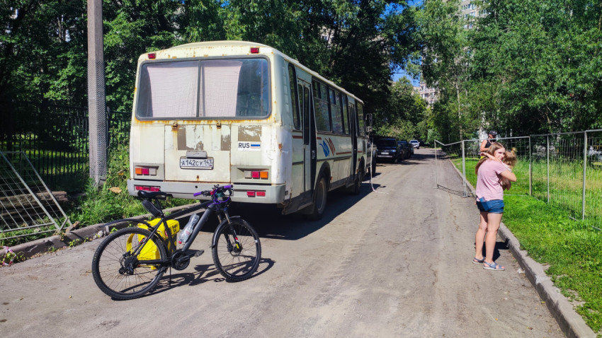 Остановившийся автобус на тенистой улице и велосипед на обочине рядом с жилой застройкой