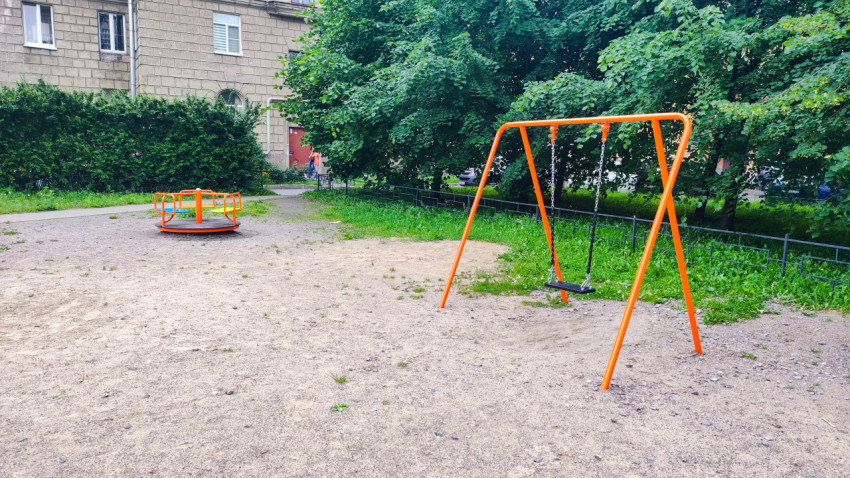 Оранжевые качели и карусель на песчаной площадке во дворе