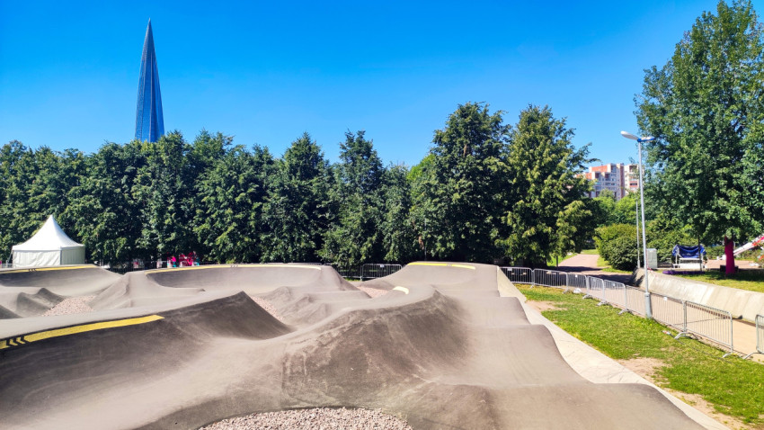 Памп-трек с серией холмов и ограждениями на фоне деревьев и Лахта Центра