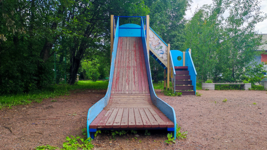 Деревянная детская горка на песчаной площадке во дворе летом