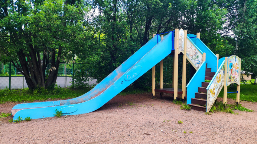 Игровой комплекс с длинной голубой горкой и лестницей под деревьями