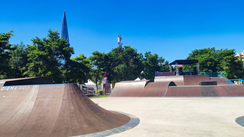 Панорама скейтпарка с фигурами для BMX и сценой на фоне зелени