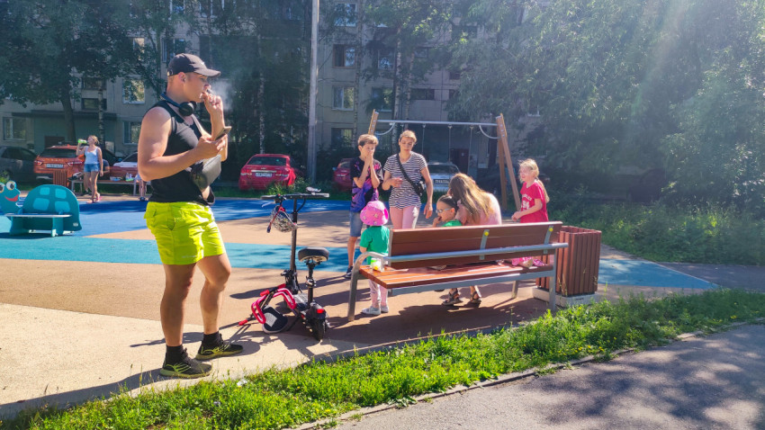 Мужчина с телефоном стоит у самоката возле детской площадки во дворе жилого дома