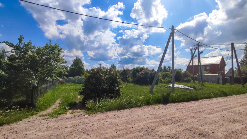 Грунтовая дорога, опоры ЛЭП и частный дом под кучевыми облаками