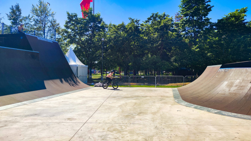 BMX-райдер едет по бетонной зоне между двумя квотерпайпами скейтпарка под флагом СССР