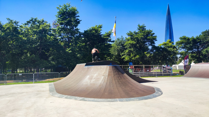 BMX-райдер стоит на верхней площадке рампы скейтпарка на фоне «Лахта Центра»
