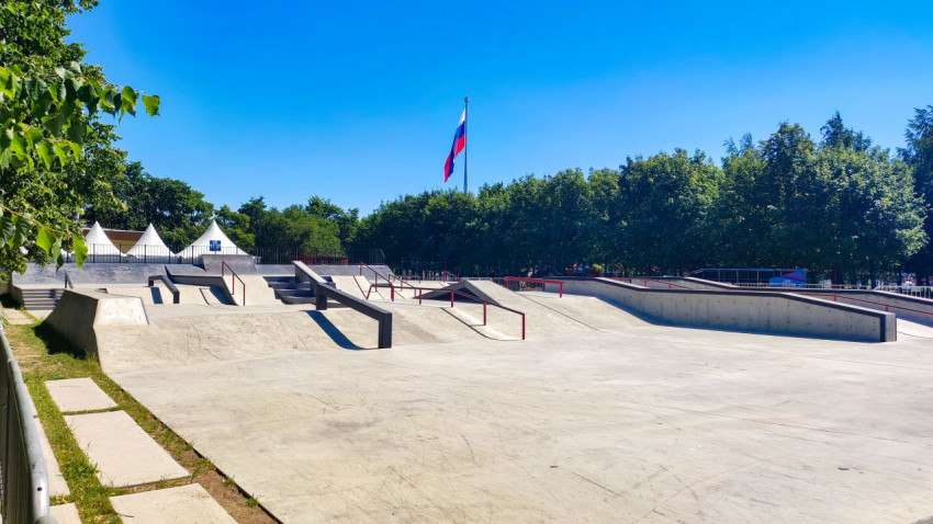 Бетонный скейтпарк с рейлами и флагштоком с флагом на фоне деревьев