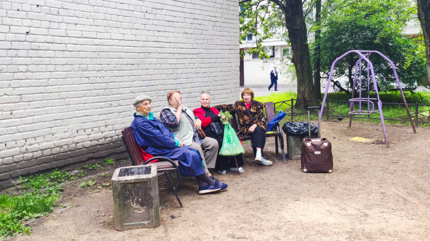 Пожилые женщины на скамейке во дворе рядом с детской площадкой и качелями