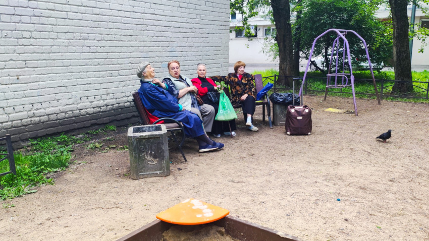 Пожилые женщины на скамейке во дворе у кирпичной стены