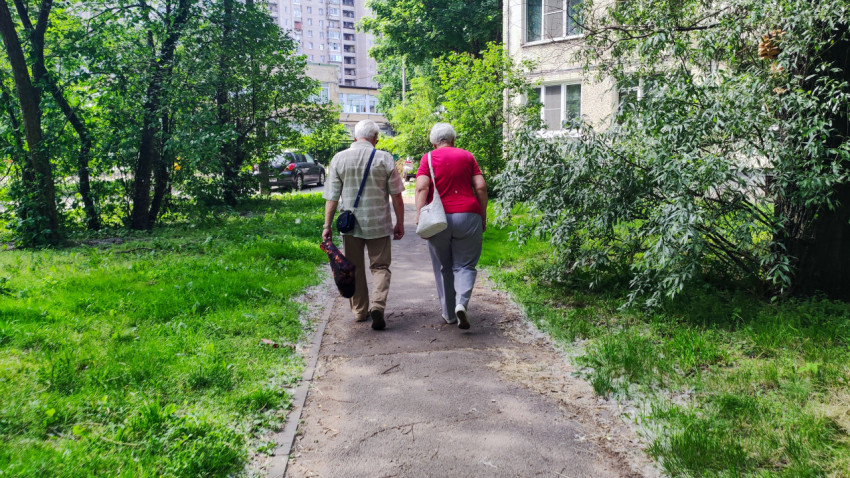 Пожилые мужчина и женщина на прогулке по дворовой дорожке среди деревьев