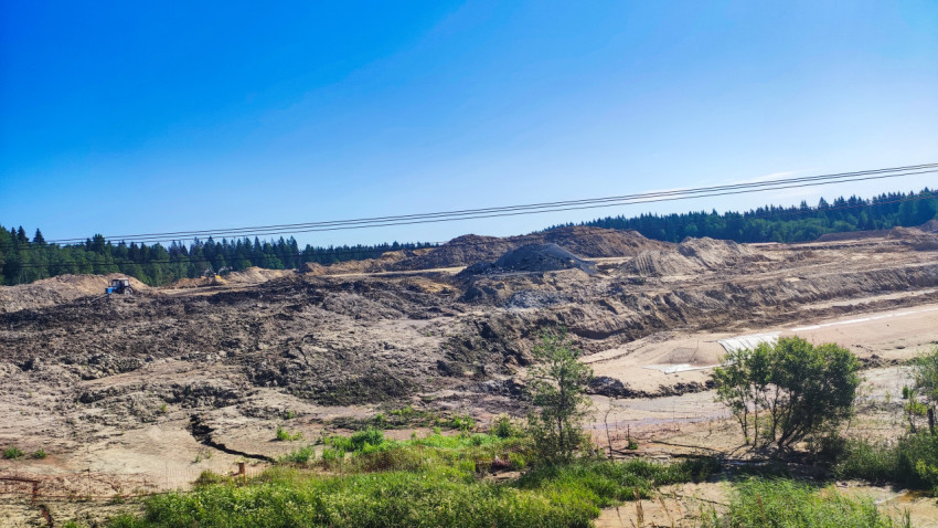 Панорама песчано-грунтового карьера с насыпями, техникой и линиями электропередачи на фоне леса