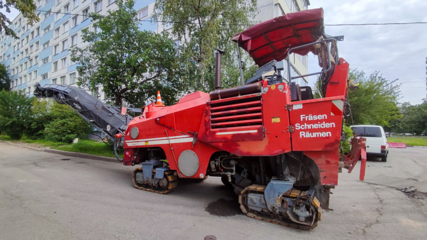 Дорожная фреза с надписью «Fräsen Schneiden Räumen» на фоне многоэтажного жилого дома