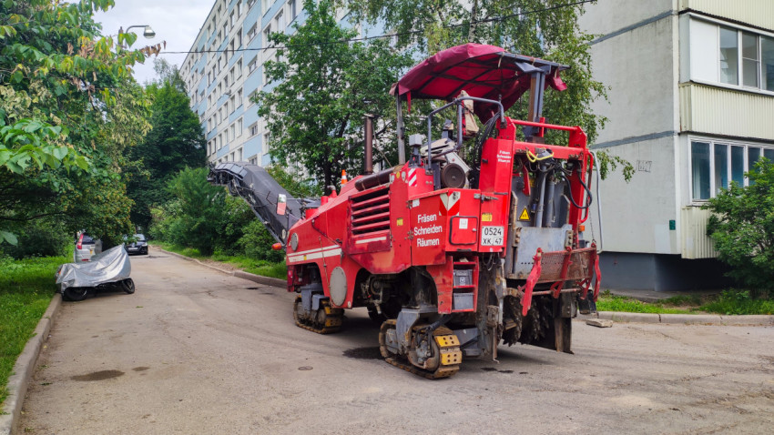 Красная дорожная фреза на гусеницах припаркована у жилого дома во дворовом проезде